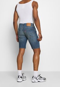 Farkkushortit keskipitkässä sinisessä, suoralinjaisessa leikkauksessa, takataskuilla ja nahkapatilla vyötäröllä. Yhdistetty valkoisten sukkien ja tenniskenkien kanssa.