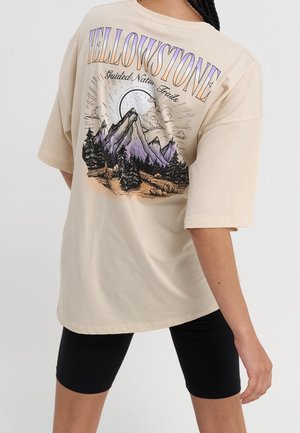 Béžové oversized tričko s grafickým motivem hor a stromů, s nápisem "YELLOWSTONE" ve fialové a oranžové barvě na zádech.