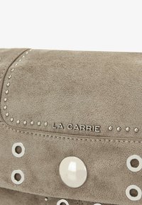 Clutch in camoscio beige con borchie argento, grande chiusura rotonda e marchio in rilievo. Texture liscia con fori decorativi e accenti.