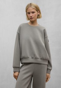Felpa grigia con scollatura rotonda, polsini a coste e orlo aderente. Realizzata in un materiale morbido, presenta una trama sottile e un design minimal.