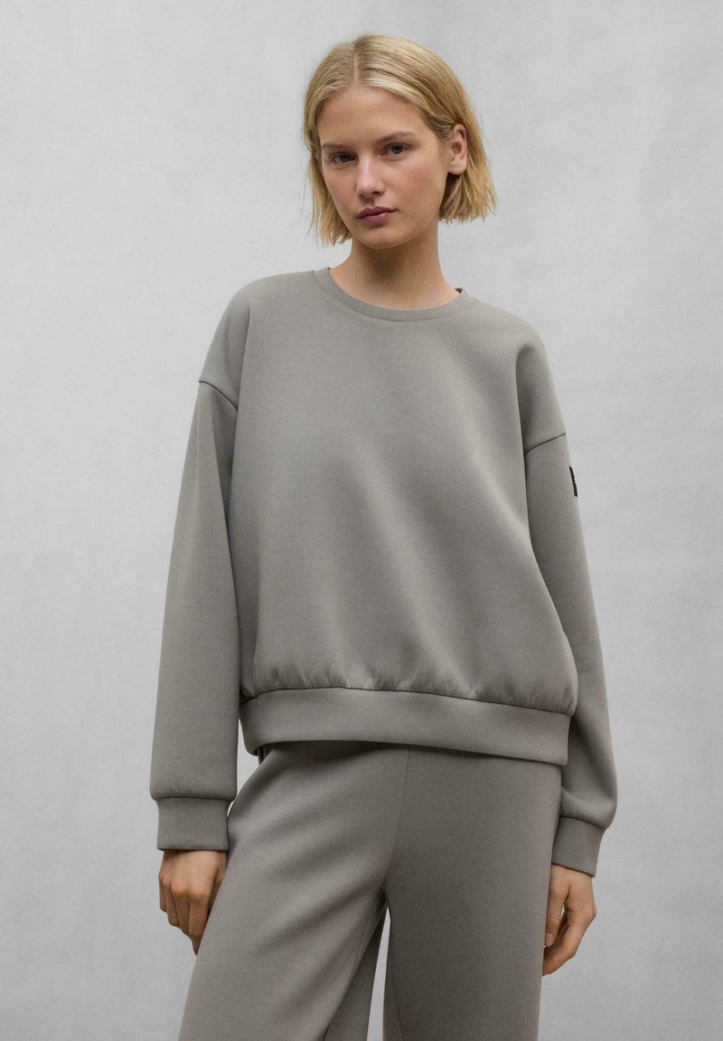 Felpa grigia con scollatura rotonda, polsini a coste e orlo aderente. Realizzata in un materiale morbido, presenta una trama sottile e un design minimal.