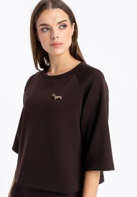 Brązowy, krótki t-shirt z krótkim rękawem i rękawami raglanowymi, z haftem przedstawiającym teksturowanego jamnika z przodu. Gładki materiał o luźnym kroju.