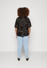 Svart skjorta med vitt streckmönster, korta ärmar och rundad nederkant, tillsammans med ljusblå skinny jeans och svarta spikade flats.