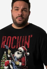 Černé tričko s dlouhým rukávem s grafikou Santy hrajícího na elektrickou kytaru a designem vánočního stromku. Text zní "ROCKIN'".