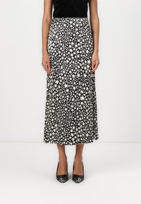 Schwarz-weißes Midi-Rock mit Sternenmuster, ausgestattet mit einem gefalteten Design und einer glatten Stofftextur, kombiniert mit schwarzen High Heels.