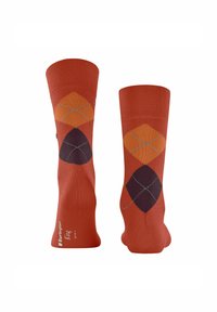 Une paire de chaussettes couleur rouille avec un motif argyle en diamants orange et violet foncé, et un petit texte près de la zone des orteils.