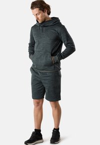 Felpa atletica grigio scuro con collo a scialle, cordoncino e tasche frontali, abbinata a pantaloni corti coordinati. Indossata con sneakers nere.