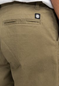 Olijfgroene katoenen shorts met een achterzak, contrasterend donker label en klassieke stiksel details. Glad textuur en rechtvallend ontwerp.
