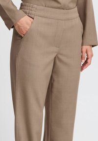 Pantaloni beige a gamba dritta con vita elastica, tasche laterali e una texture morbida e tessuta. Vestibilità sartoriale con dettagli di cucitura minimi.