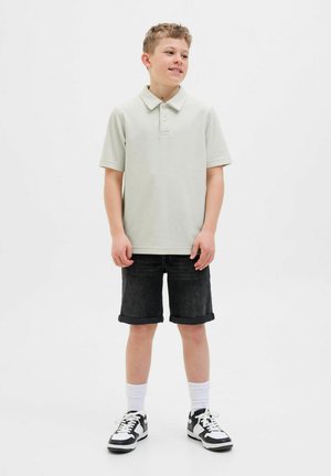 Ljusgrå polo med krage, matchad med svarta denimshorts. Modellen bär vita strumpor och svarta sneakers med vita detaljer.