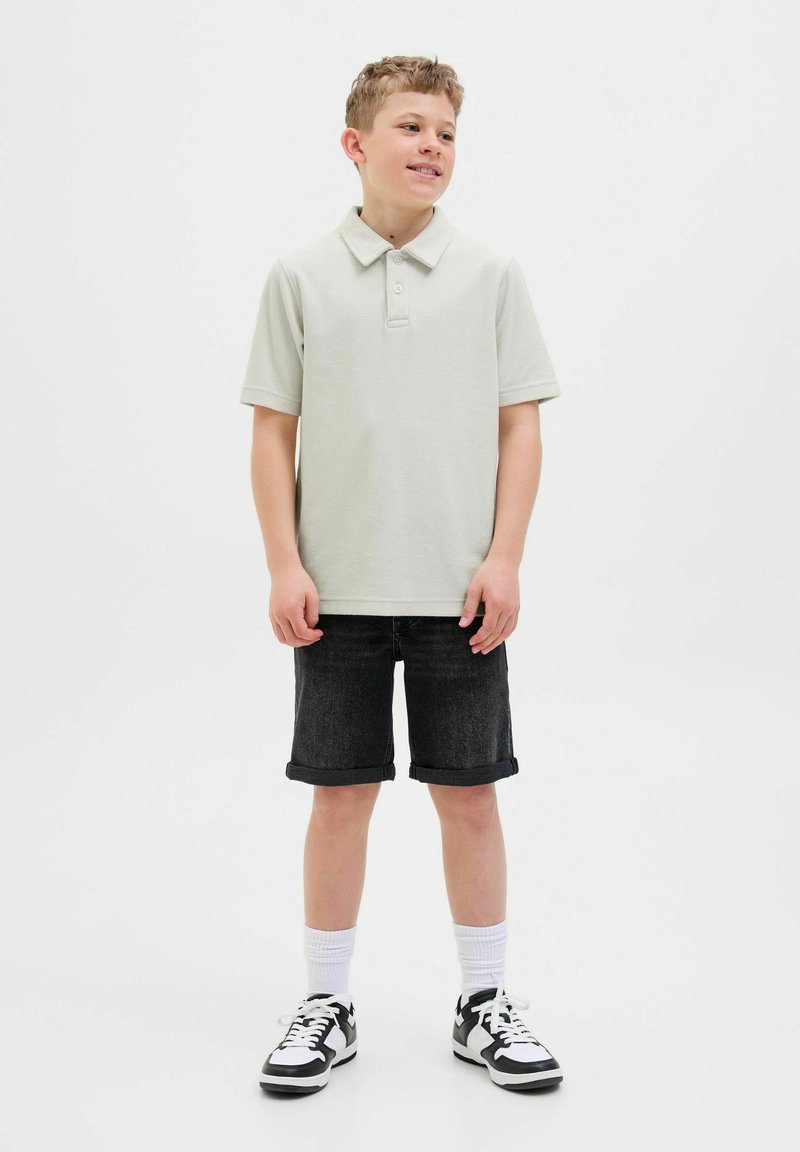 Ljusgrå polo med krage, matchad med svarta denimshorts. Modellen bär vita strumpor och svarta sneakers med vita detaljer.