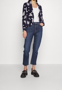 Mörkblå och grå mönstrad blazer med öppen krage, ihopsatt med högmidjade jeans i denim och svarta klumpiga loafers. Slät tygtextur är påtaglig.