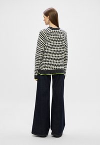 Pulover tricotat în alb și negru, cu un model geometric; mâneci lungi, guler și manșete cu nervuri, având accente verzi strălucitoare la tiv.