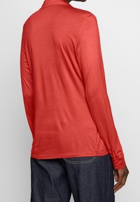 Camicia a maniche lunghe color corallo, caratterizzata da una texture morbida e liscia con vestibilità comoda e polsini con bottoni, abbinata a pantaloni in denim blu scuro.