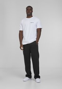 White short-sleeve t-shirt with black text, paired with black trousers and white sneakers. Simple design, solid colors, smooth texture.