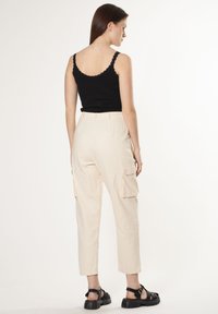 Zwarte tanktop met kantafwerking, crèmekleurige cargobroek met zijvakjes, cropped lengte en zwarte sandalen met dikke zolen.
