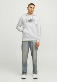 Lichte grijze hoodie met een voorzak, trekkoorden en grafisch ontwerp. Gecombineerd met lichtblauwe jeans en witte sneakers.