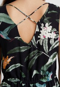 Mono floral con fondo oscuro, que presenta una espalda en V profunda, tirantes cruzados y hojas y flores vibrantes en verde, rosa y naranja.