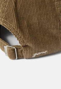Gorra de pana marrón con tejido texturizado, correa ajustable y logo bordado en blanco. Presenta una corona estructurada y visera curva.