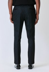 Black patterned trousers with a textured finish, featuring a slim fit. Back view shows two pockets and sleek, shiny black shoes.