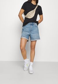 Černé tričko, světle modré džíny šortky s ohrnutými manžetami, béžová krosbody taška a bílé tenisky s neonovými akcenty. Hladké textury.