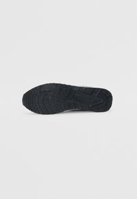 Semelle de chaussure en caoutchouc noir avec un motif de bande de roulement texturé, comportant des rainures et des crêtes pour l'adhérence. Le matériau est durable et conçu pour la traction.