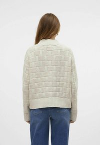 Cremefärgad stickad tröja med ett strukturerat korgvävsmönster, ribbad nederkant och avslappnad passform. Kombineras med blå vida jeans.