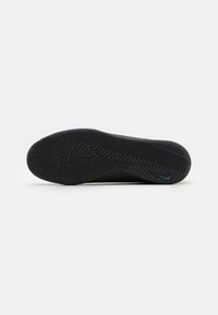 Semelle de chaussure de sport noire en caoutchouc texturé, présentant un design courbé et des motifs de semelle distincts pour une meilleure traction. Accent d'un petit logo.