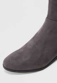 Grå mokkasin-ankelstøvel med slank silhuett, spiss tå og en minimal svart yttersåle. Jevn tekstur, uten synlige mønstre eller dekorasjoner.