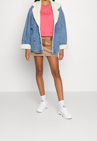 Jeansjacka med faux shearling-krage, rosa Nike-tröja, beige mini-skjorta och vita sportskor med synlig luftkuddsystem.