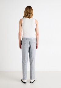 Canotta bianca a costine e pantaloni grigi chiari su misura con un sottile motivo a quadri. I pantaloni presentano due tasche posteriori e scarpe eleganti e minimaliste.
