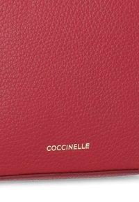 Borsa a mano rossa in pelle con superficie texturizzata, caratterizzata da un logo dorato "Coccinelle" nell'angolo in basso a destra. Forma rettangolare.
