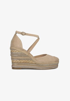 Alpargatas de cuña de ante beige con una suela intermedia de yute trenzado, correa en el tobillo y punta redondeada. Presenta acentos metálicos decorativos.