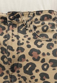 Τζιν παντελόνια με λεοπάρ σχέδιο που διαθέτουν μπεζ φόντο με μαύρες και καφέ κηλίδες, κλείσιμο με κουμπί και μια μικρή ετικέτα μάρκας στη ζώνη μέσης.