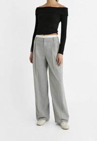 Czarna bluzka off-shoulder z długim rękawem połączona z jasnoszarymi spodniami typu palazzo z plisowanym wzorem i elastyczną talią. W zestawie białe sneakersy.