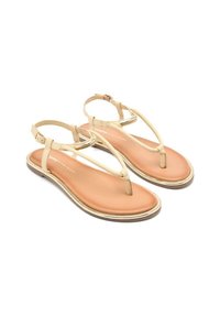 Sandalias beige con diseño de tira en T, material suave y suela acolchada en tono tostado. Presentan una delgada correa para el tobillo con hebilla y detalles metálicos.
