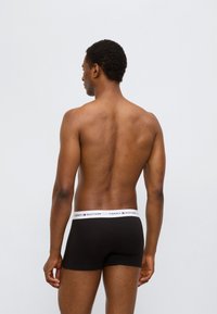 Μαύρα ανδρικά μπόξερ με λευκή ελαστική μέση που φέρει το λογότυπο "TOMMY HILFIGER", εμφανιζόμενα από πίσω. Λείο ύφασμα.