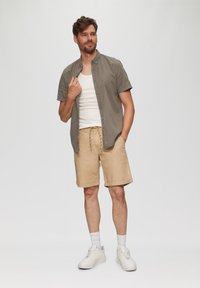Korte mouwen overhemd met grijs patroon, witte tanktop, tan korte broek met koord, en witte sneakers met een textuurlopende zool.