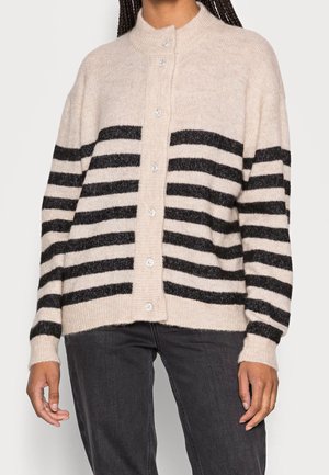 Beige button-up cardigan with black horizontal stripes worn with black pants; ribbed cuffs and collar visible.