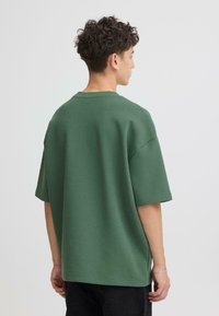 T-shirt oversize à manches courtes de couleur vert forêt, en mélange de coton avec une texture lisse. Doté d'un col rond et d'épaules tombantes.