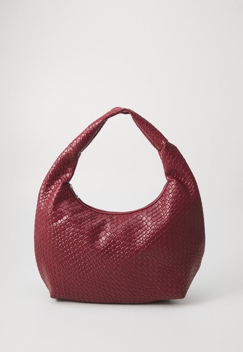 Sac hobo en cuir tressé rouge avec une anse courbée unique et une fermeture éclair, debout contre un fond uni.