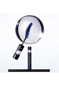 Schwarzes Mascara-Röhrchen mit blauen Akzenten, ausgestattet mit einer großen, klaren sphärischen Linse, die einen Wimpernbürstenaufsatz mit blauen Borsten zeigt, der sich über einem schwarzen Grund befindet.