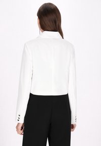 Witte cropped blazer met lange mouwen, voorzien van een notch-kraag en knoopmanchetten. Gecombineerd met zwarte broek, wat een nette, op maat gemaakte uitstraling geeft.