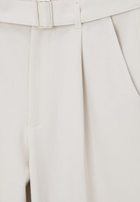 Pantalons en tissu gris clair avec une ceinture à boucle en argent, design à plis à l'avant et poches latérales. Texture lisse avec une coupe ajustée.