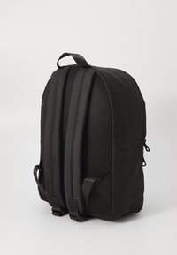 Sac à dos noir avec des panneaux latéraux en mesh et des sangles ajustables, présenté de côté sur un fond blanc uni.