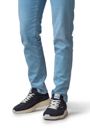 Sneakers mit einem dunkelblauen Veloursleder-Obermaterial, weißen Schnürsenkeln und einer cremefarbenen Sohle. Blaue Jeans mit schmaler Passform und leicht ausgewaschenem Finish.