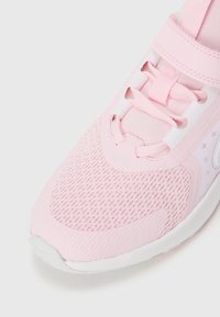 Chaussure de sport rose clair avec tige en mesh, fermeture à lacets et semelle en caoutchouc. Caractéristiques : superpositions lisses et motif perforé pour la respirabilité.