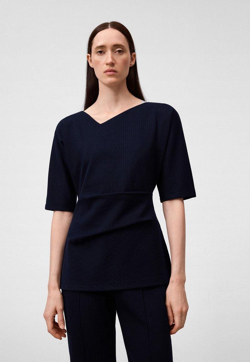 Granatowa bluzka z dekoltem w serek, krótkimi rękawami, lekko teksturowana, o strukturalnym kroju, w połączeniu z dopasowanymi spodniami.