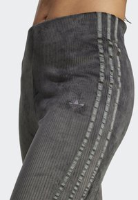 Gray corduroy leggings featuring three vertical stripes and an embroidered logo on the thigh. Textured fabric with a ribbed pattern.