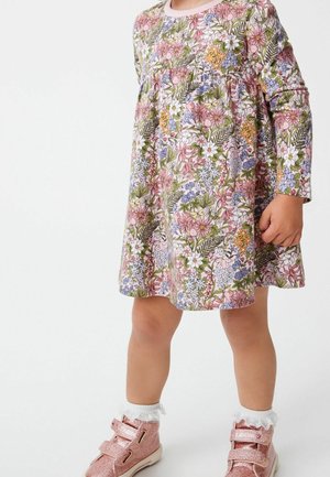 Niña con un vestido floral de manga larga con patrones en rosa, blanco y verde, calcetas blancas con volantes y zapatos rosas brillantes.